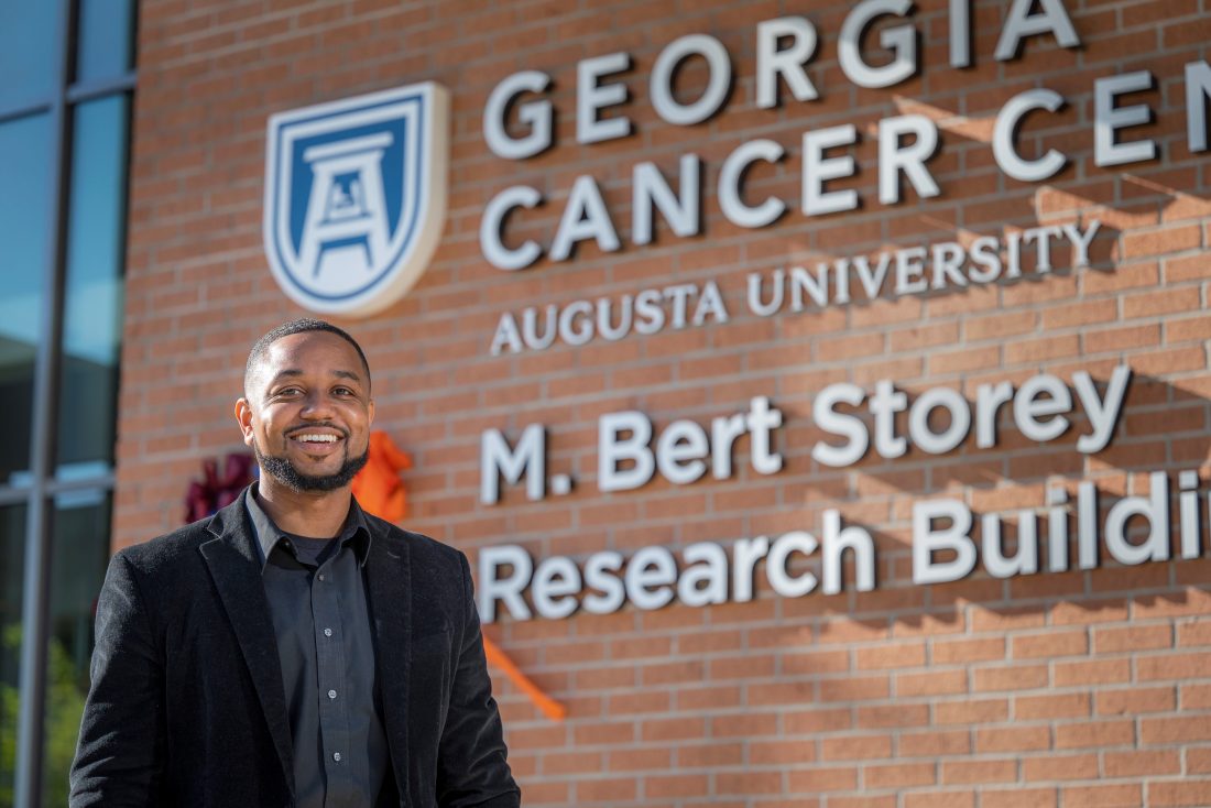 Man in black jacket stands in front of Georgia Cancer Center
