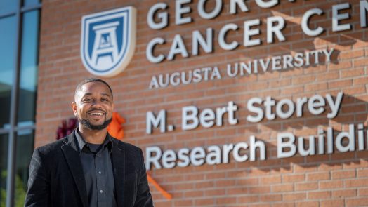 Man in black jacket stands in front of Georgia Cancer Center