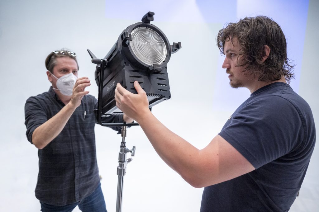 Two men standing and working with camera and lighting equipment.