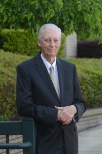 man in navy suit leans on railing