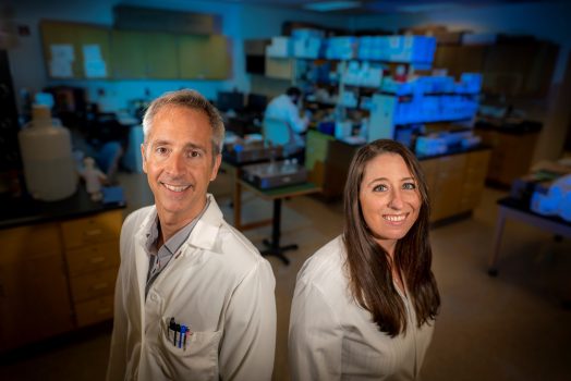 Man and woman wearing white coats stand back to back