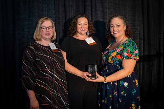 Three women stand in row holding award