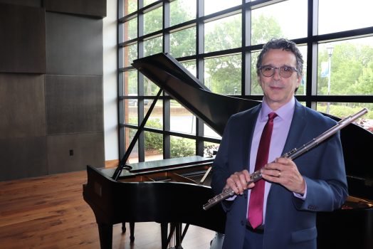 man stands in front of piano, holding a flute