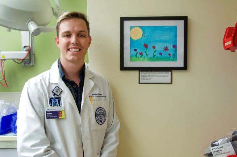 man in white coat in front of children's drawing