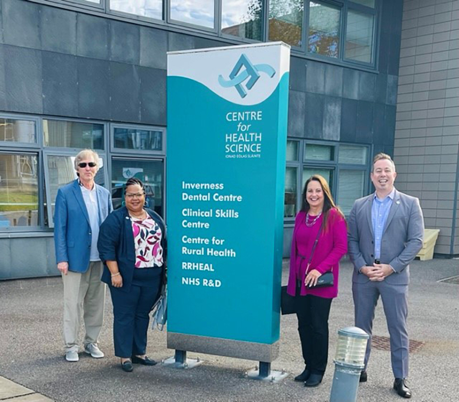 Four people, two women and two men, stand outside a building next to a tall sign for the Centre for Health Science.