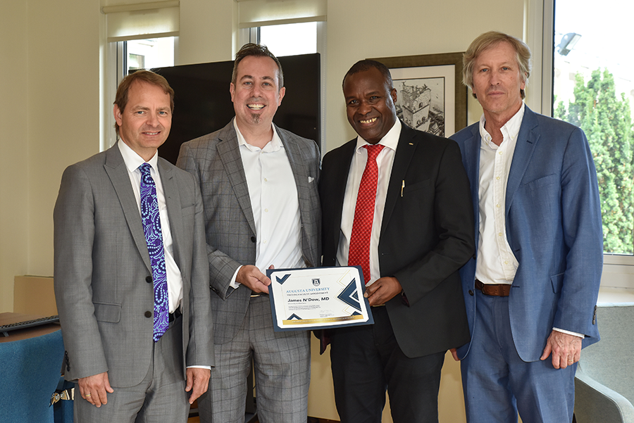 four men stand together while the middle two hold up a certificate