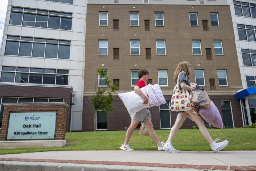 two women carrying bags walk by the front of a residence hall