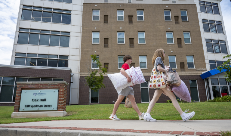 two women carrying bags walk by the front of a residence hall