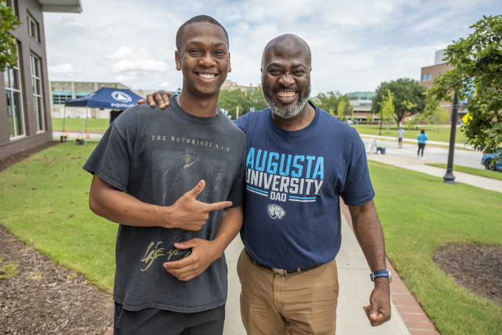 man standing beside his father; father is wearing "Augusta University Dad" T-shirt