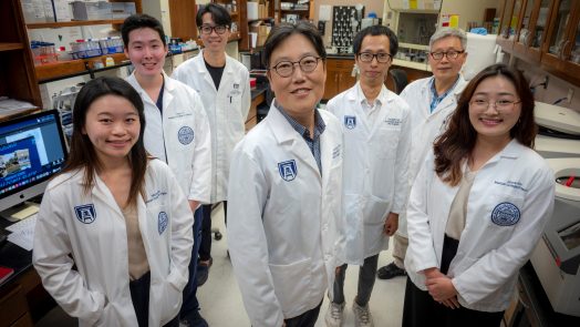 Group of researchers in white coats stand in circle in lab