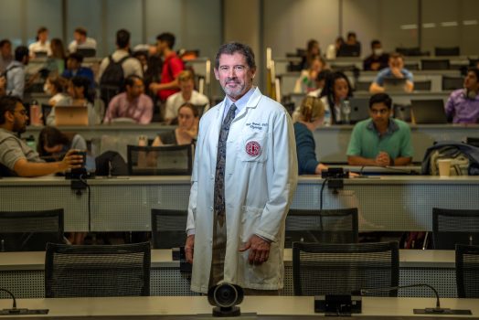 Man in white coat stands in front of classroom of students