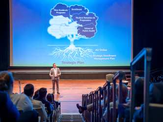 man gives presentation on stage in large auditorium