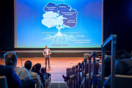man gives presentation on stage in large auditorium