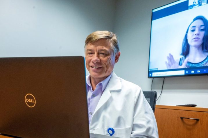 Man looks at laptop computer while woman on screen is projected behind him