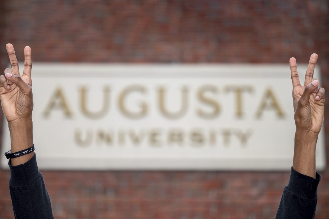 Hands in front of Augusta University sign