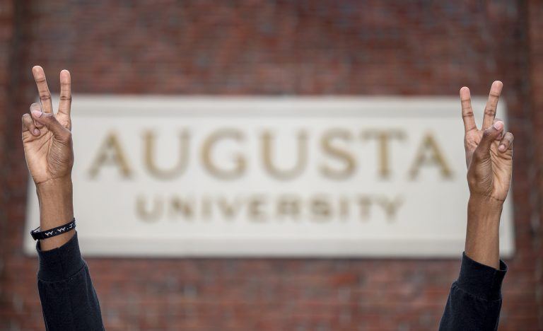 Hands in front of Augusta University sign