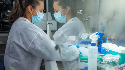 woman wearing surgical mask looks through glass window while sorting testing equipment