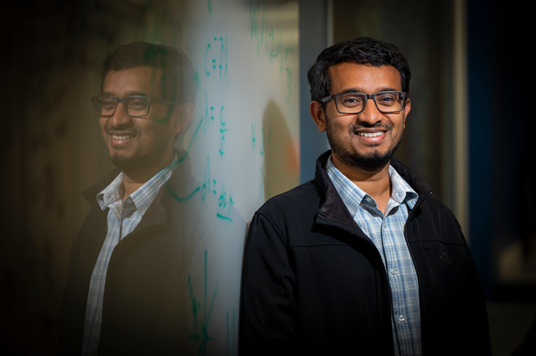 man with glasses in jacket standing in front of dry erase board