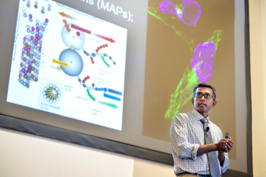 Man in white tie and shirt stands in front of projector screen