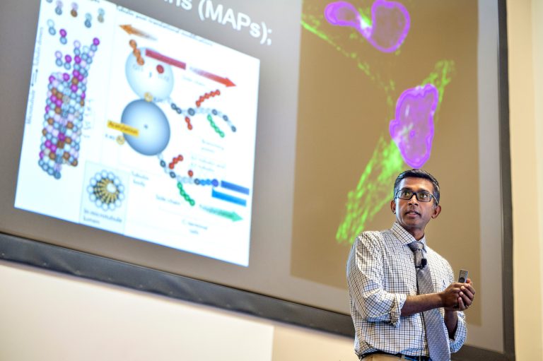 Man in white tie and shirt stands in front of projector screen