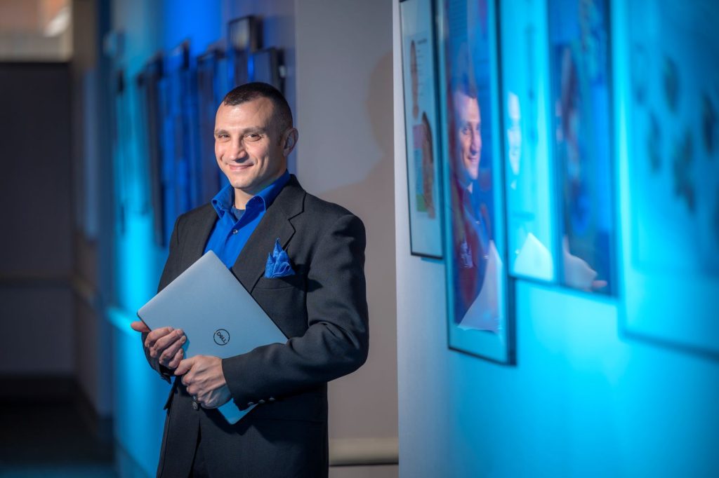 man standing in hallway, holding laptop