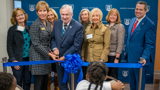 eight people stand behind a ribbon as two hold large scissors to cut the ribbon during a ceremony