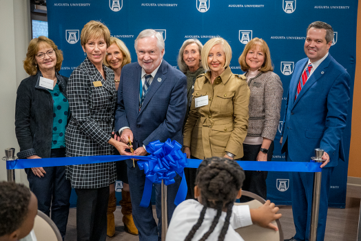 eight people stand behind a ribbon as two hold large scissors to cut the ribbon during a ceremony