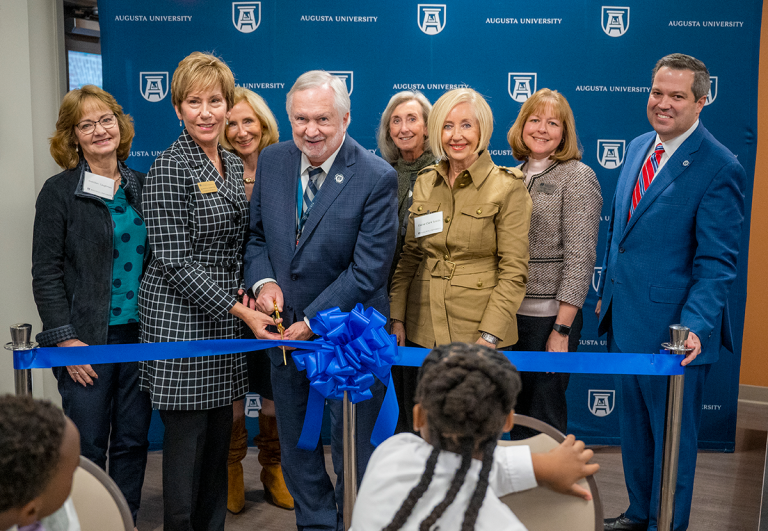eight people stand behind a ribbon as two hold large scissors to cut the ribbon during a ceremony
