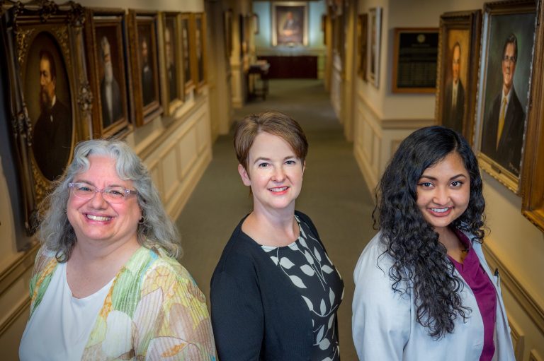 Three women stand shoulder to shoulder in hallway looking at the camera
