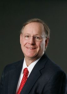 Man in navy suit and red tie smiles at camera