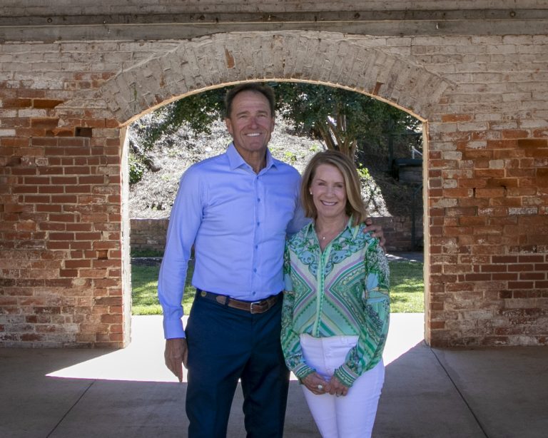 two people standing outdoors near a brick archway