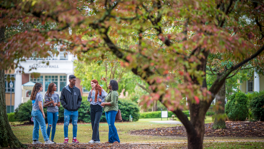 group of five college students stand together outside under trees