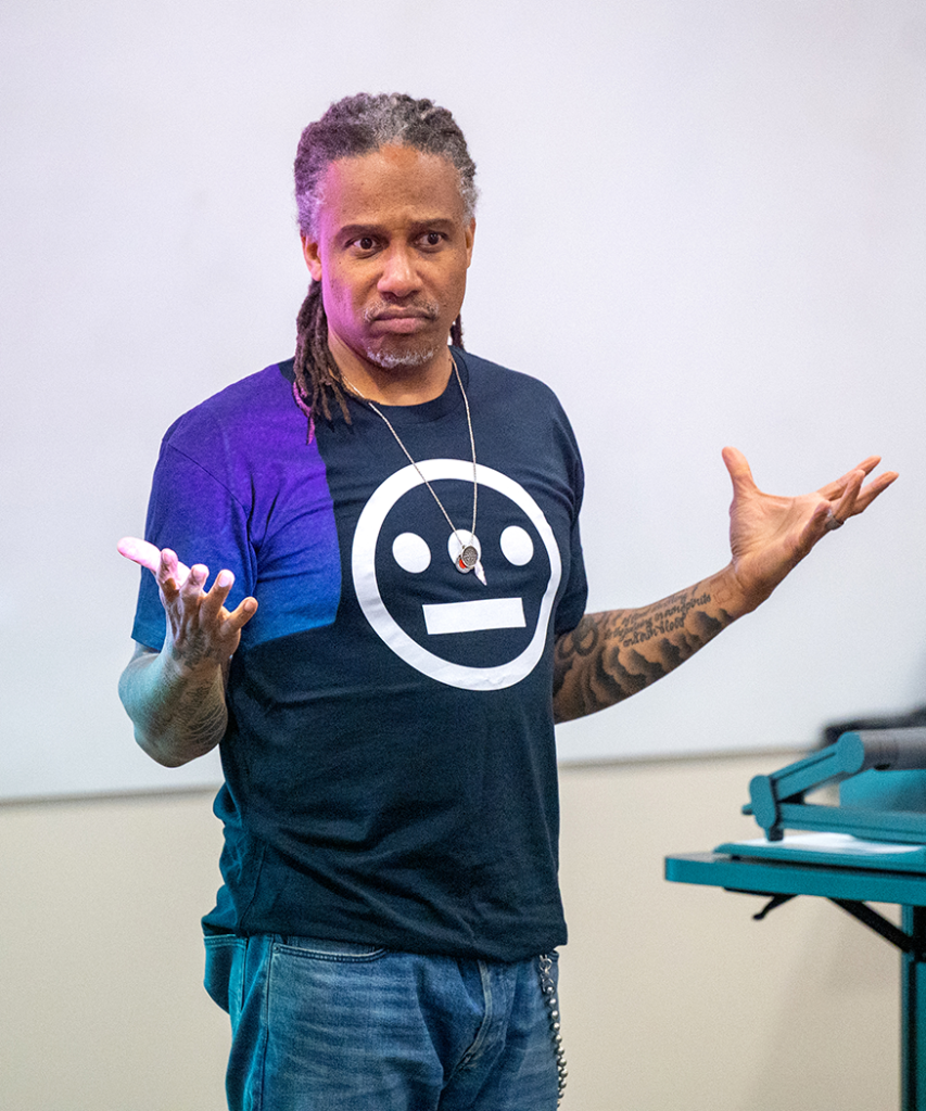 man holds his hands out to the side as he asks a question during a presentation in front of a projector screen