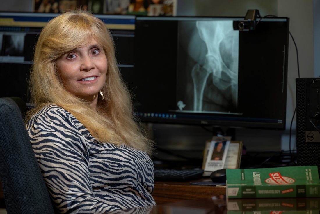 woman with long blonde hair looks at camera while sitting in front of a hip X-ray