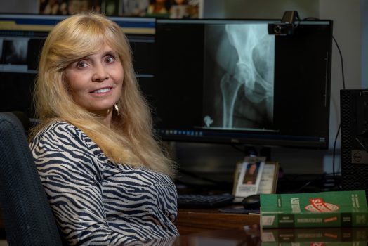 woman with long blonde hair looks at camera while sitting in front of a hip X-ray