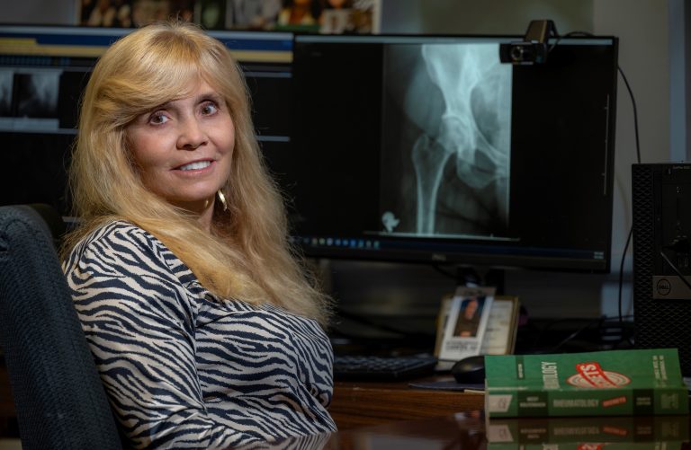 woman with long blonde hair looks at camera while sitting in front of a hip X-ray
