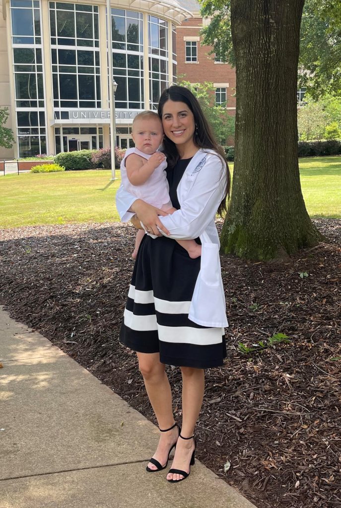 woman in white coat standing outside, holding a baby