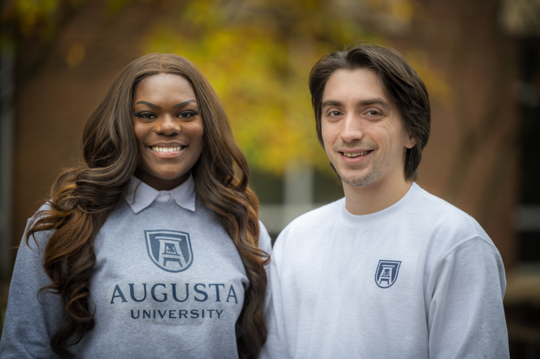 woman and man smiling outdoors, both wearing Augusta University shirts