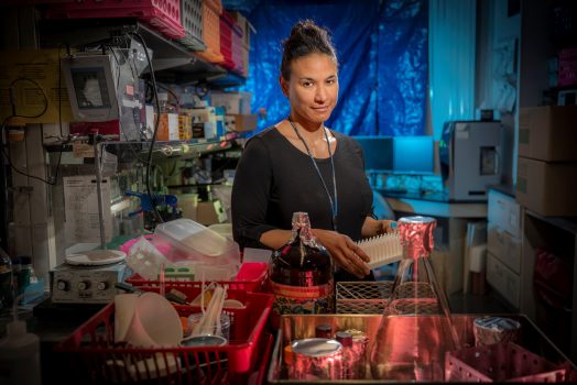 Woman in black shirt with hair in bun stands in front of lab equipment