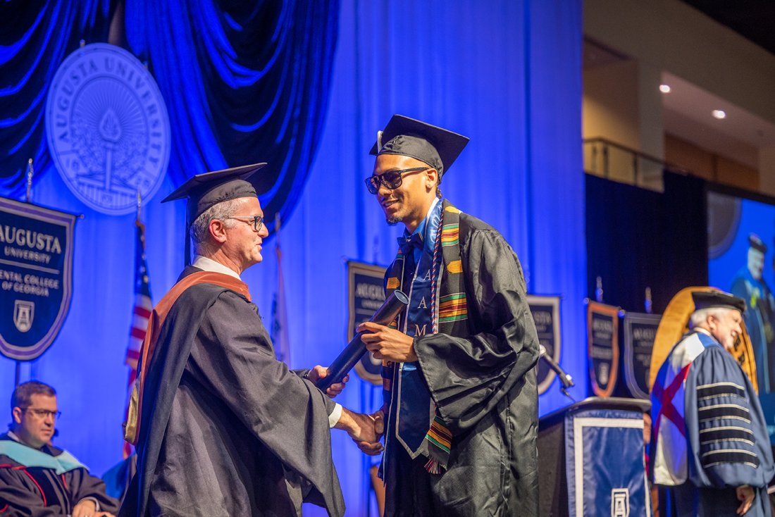 man shaking hands with a chairperson on graduation stage