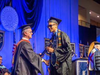 man shaking hands with a chairperson on graduation stage