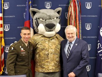 Army major general and university president stand with jaguar mascot.