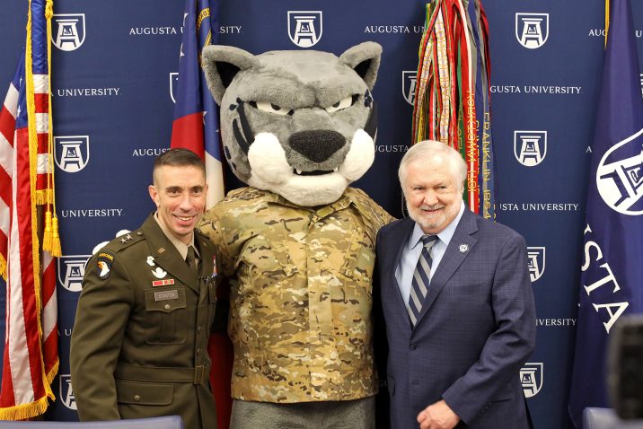 Army major general and university president stand with jaguar mascot.