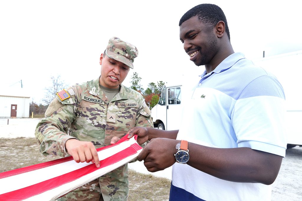 A soldier in uniform shows a man how to fold the American flag.