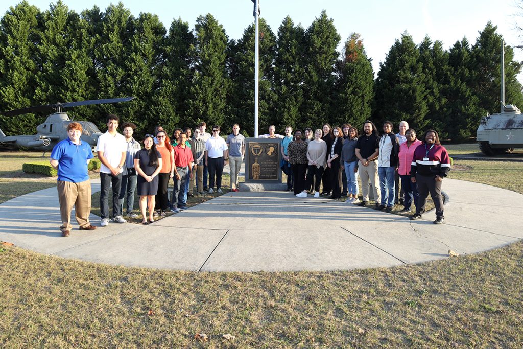 large group of people stand outside in front of a memorial plaque