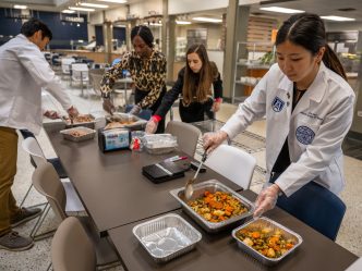 Students stand around table spooning food into containers