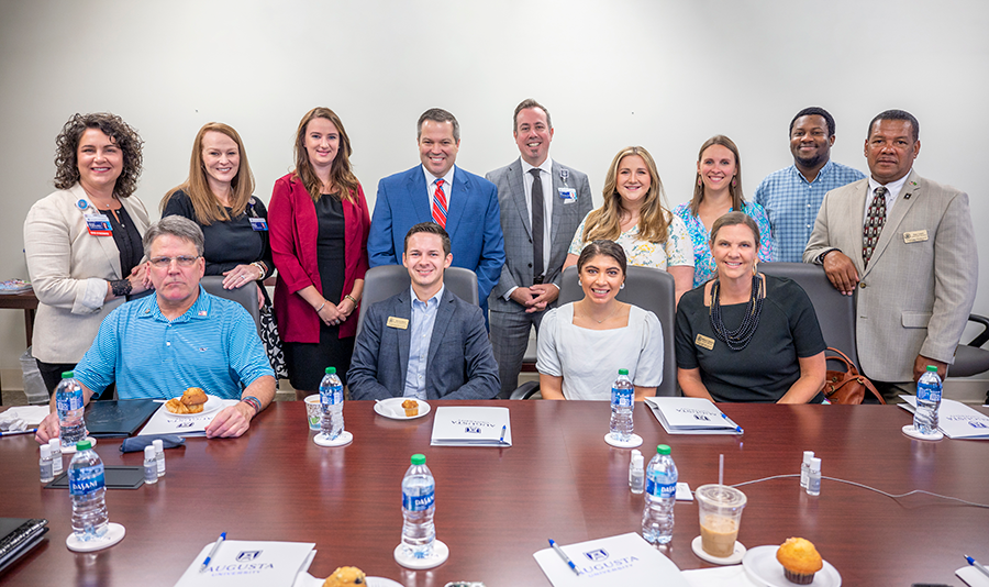 large group of people gather around a table for a photo op during breakfast in a large conference room