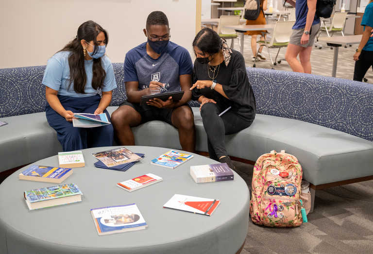 tree students sitting on round couch watching a video shown on a phone