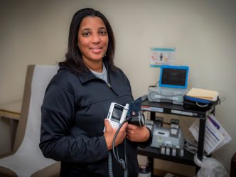 Woman in black jacket stands in clinic room holding dopplar machine