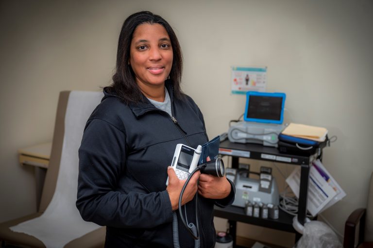 Woman in black jacket stands in clinic room holding dopplar machine